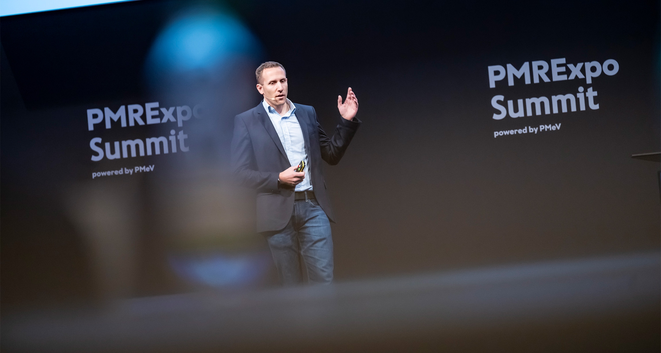 A dynamic speaker passionately engages the audience at the PMRExpo Summit, set against an eye-catching backdrop showcasing the event's branding.