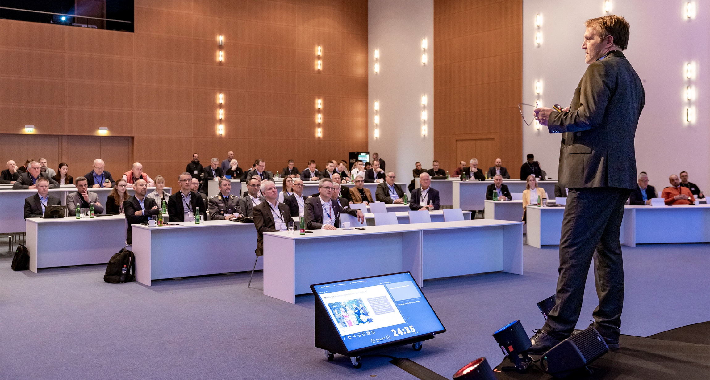 A dynamic speaker captivates an engaged audience in a brightly lit conference hall, where a timer counts down on a prominent screen to add urgency to the presentation.