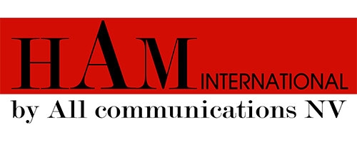 The image prominently showcases the HAM International logo by All Communications NV, featuring the brand name in bold letters against a striking red background, symbolizing the company's commitment to innovative GSM indoor coverage solutions that will be demonstrated at PMRExpo.