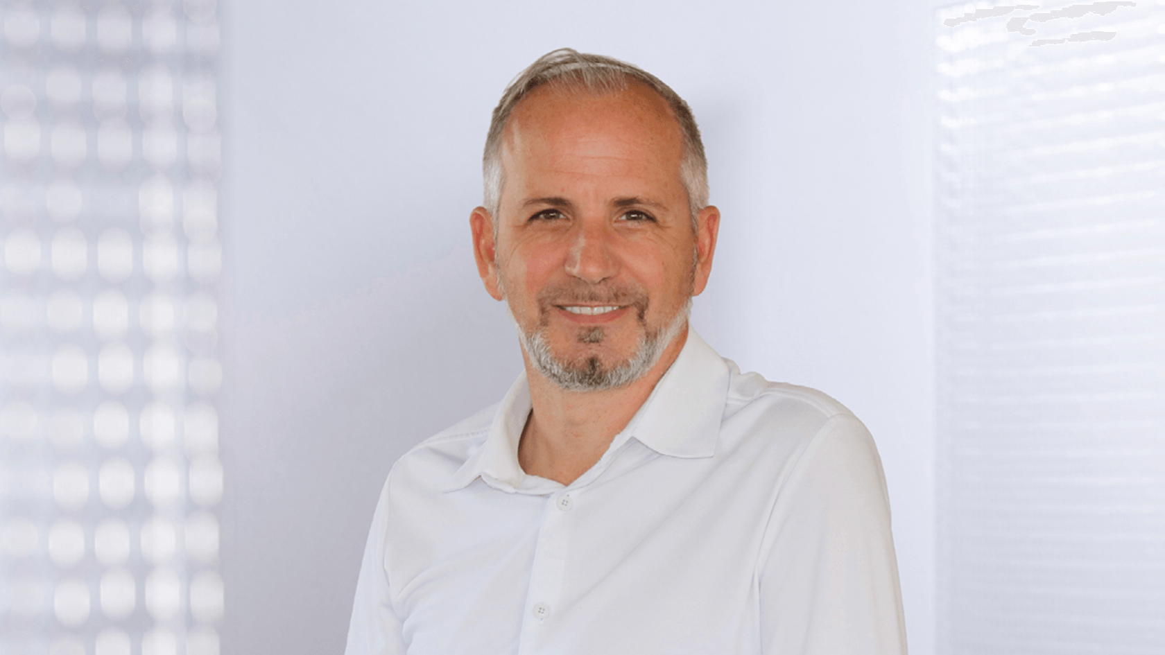 A smiling Javier Esparza, the Sales Director for Europe at RugGear, stands in a light-colored shirt against a soft, neutral background, embodying the spirit of innovation and partnership that defines PMRExpo.